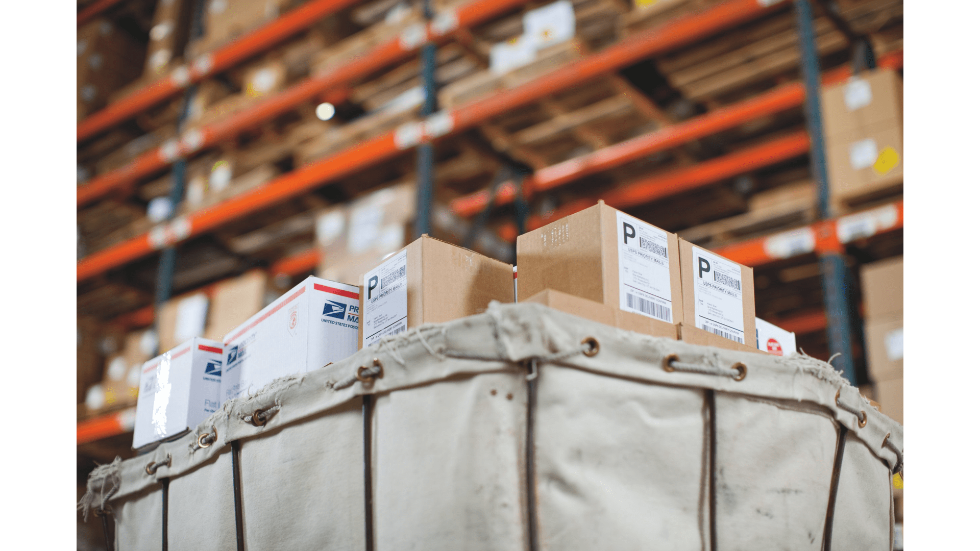 A warehouse setting with shelves filled with stacked boxes in the background. In the foreground, a canvas shipping cart contains packages with printed shipping labels, ready for dispatch. The scene represents logistics, order fulfilment, and efficient shipping processes.